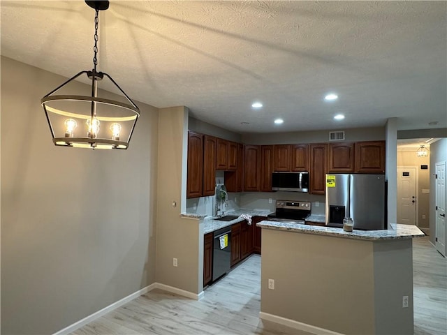 kitchen featuring light wood-type flooring, light stone counters, stainless steel appliances, pendant lighting, and a kitchen island