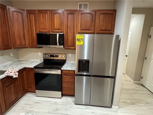 kitchen with light stone countertops, appliances with stainless steel finishes, and light hardwood / wood-style flooring