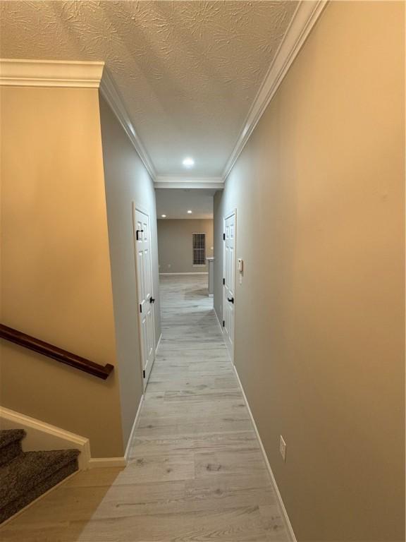 corridor featuring a textured ceiling, light hardwood / wood-style floors, and ornamental molding