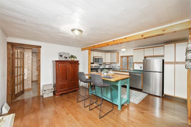 kitchen with a kitchen bar, appliances with stainless steel finishes, a kitchen island, light hardwood / wood-style floors, and white cabinetry