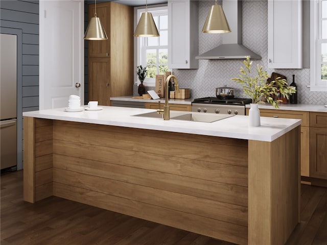 kitchen with a kitchen island with sink, dark wood-type flooring, sink, hanging light fixtures, and wall chimney exhaust hood