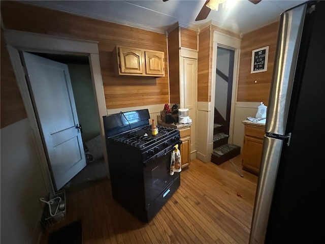 kitchen featuring stainless steel fridge, light brown cabinetry, black range with gas cooktop, hardwood / wood-style floors, and wood walls