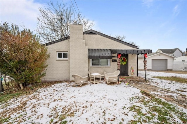 snow covered back of property featuring an outdoor structure and a garage