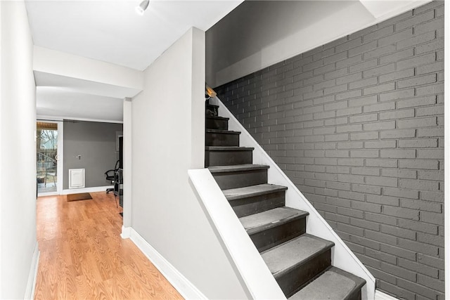 stairway featuring brick wall and wood-type flooring