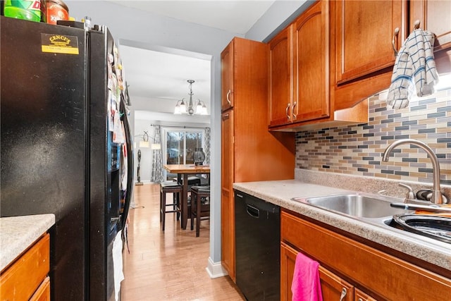 kitchen featuring black appliances, sink, decorative light fixtures, a notable chandelier, and light hardwood / wood-style floors