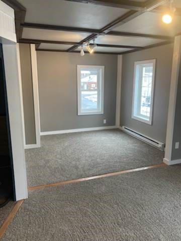 carpeted spare room with coffered ceiling, a baseboard radiator, and beam ceiling