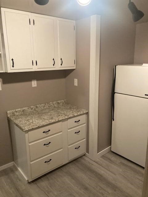 kitchen featuring white cabinets, white refrigerator, light hardwood / wood-style floors, and light stone countertops