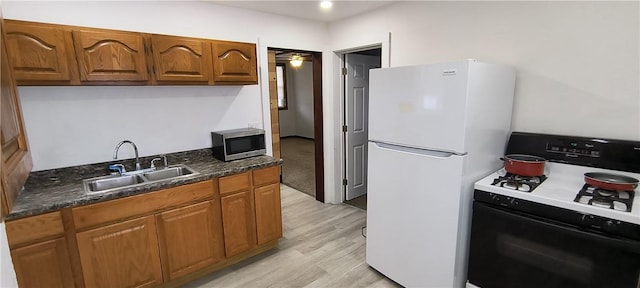 kitchen with white refrigerator, sink, gas range oven, ceiling fan, and light hardwood / wood-style flooring