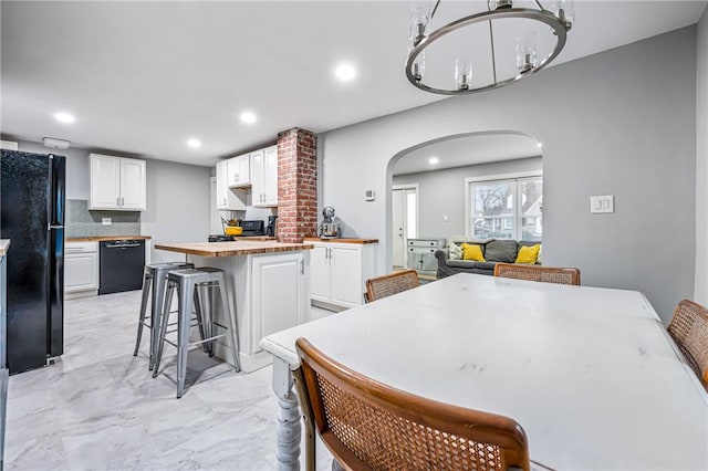 kitchen featuring a center island, a kitchen breakfast bar, butcher block countertops, white cabinets, and black appliances