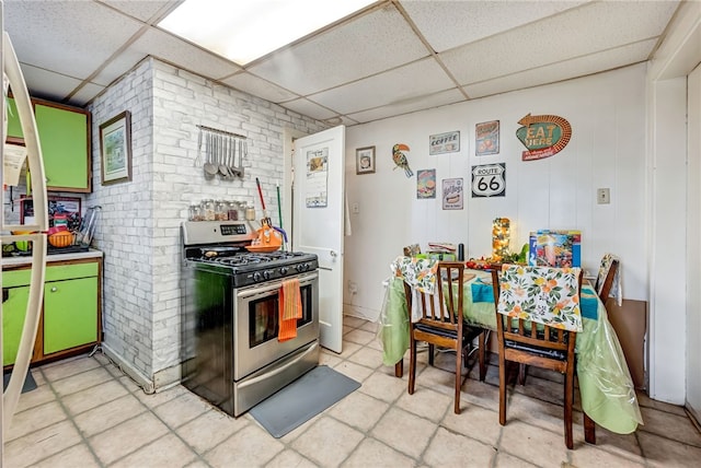 kitchen with a drop ceiling, stainless steel range with gas cooktop, brick wall, and green cabinetry