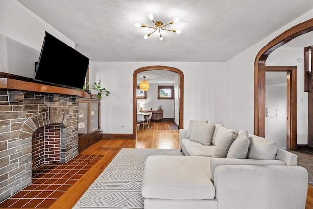 living room with dark hardwood / wood-style floors, a stone fireplace, a textured ceiling, and a chandelier