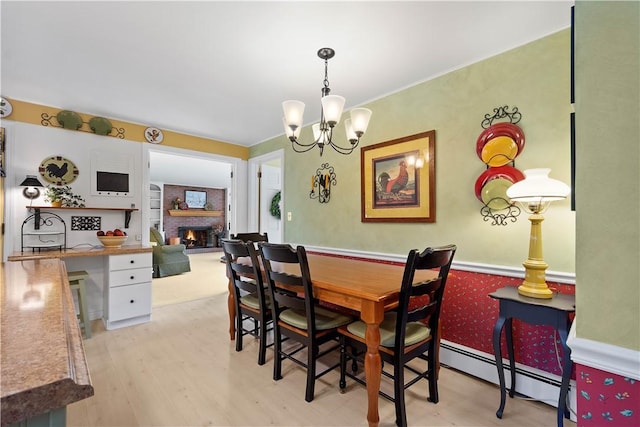 dining area featuring a brick fireplace, a chandelier, a baseboard heating unit, and light hardwood / wood-style flooring