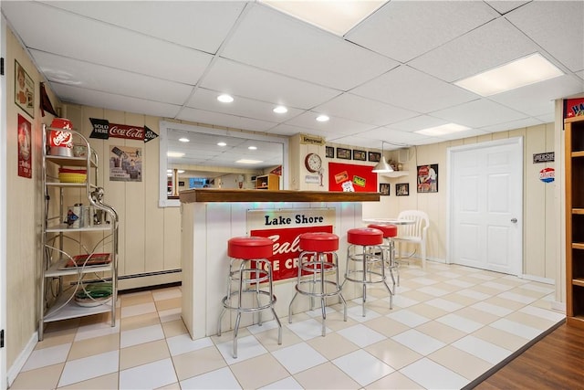 interior space with a paneled ceiling, kitchen peninsula, a kitchen breakfast bar, and baseboard heating