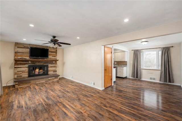 unfurnished living room with ceiling fan, a stone fireplace, and dark wood-type flooring