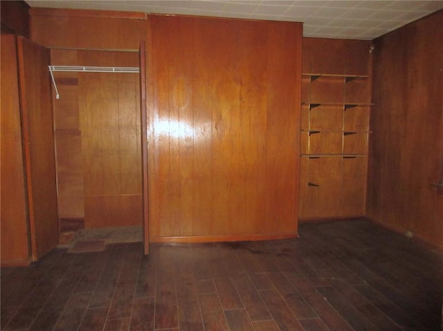 unfurnished bedroom with dark hardwood / wood-style flooring, a drop ceiling, a closet, and wood walls