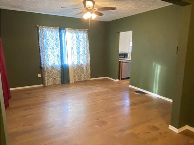 spare room featuring ceiling fan, light wood-type flooring, and a textured ceiling