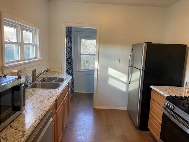 kitchen with light stone counters, sink, light hardwood / wood-style floors, and appliances with stainless steel finishes