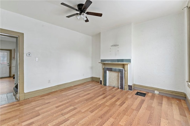 unfurnished living room featuring ceiling fan, a fireplace, visible vents, wood finished floors, and baseboards