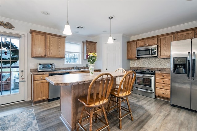 kitchen with a kitchen bar, appliances with stainless steel finishes, a center island, dark hardwood / wood-style floors, and hanging light fixtures