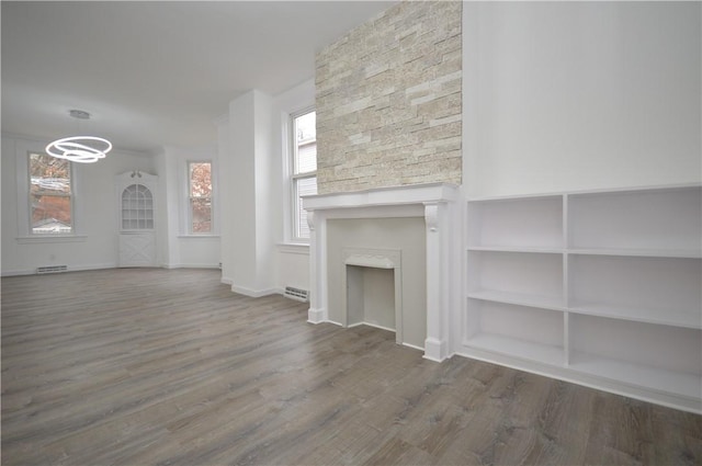 unfurnished living room with built in shelves, a stone fireplace, and dark wood-type flooring