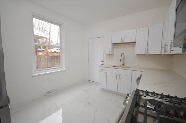 kitchen featuring white cabinets, sink, decorative backsplash, light stone countertops, and stainless steel range with gas stovetop