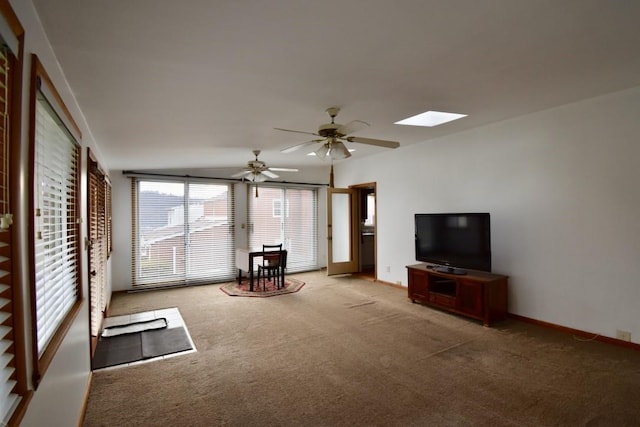 unfurnished living room with ceiling fan, a skylight, and light colored carpet