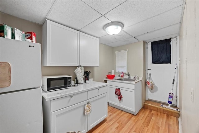 kitchen with white fridge, white cabinets, light hardwood / wood-style floors, and a paneled ceiling