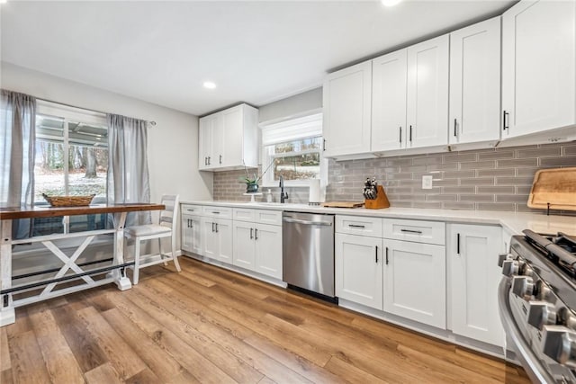 kitchen with tasteful backsplash, white cabinets, light hardwood / wood-style floors, and appliances with stainless steel finishes