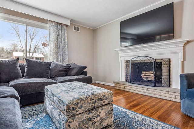 living room featuring hardwood / wood-style flooring, a stone fireplace, and crown molding