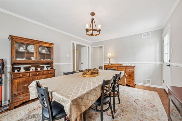 dining room with hardwood / wood-style floors, ornamental molding, and a notable chandelier