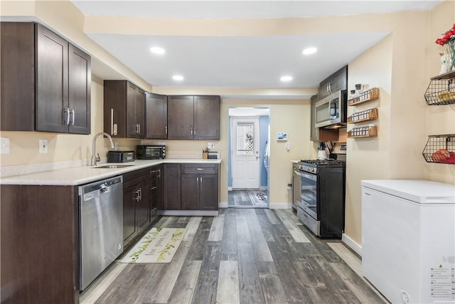 kitchen with appliances with stainless steel finishes, dark brown cabinets, dark wood-type flooring, and sink