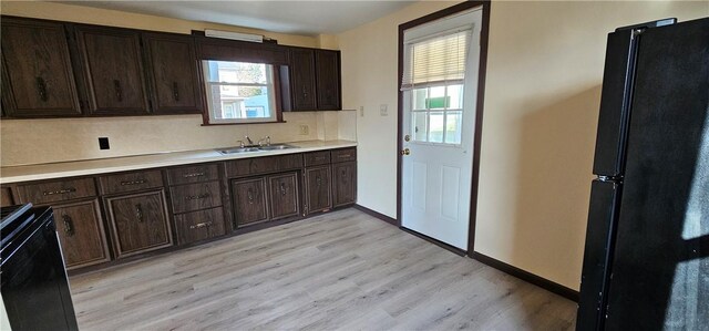 kitchen with sink, black appliances, dark brown cabinets, and light wood-type flooring