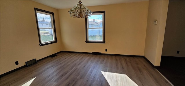 spare room with an inviting chandelier and dark wood-type flooring