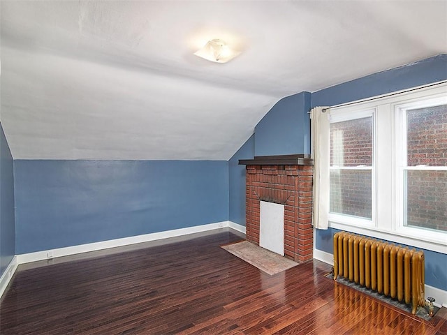 additional living space with a fireplace, vaulted ceiling, radiator, and dark wood-type flooring