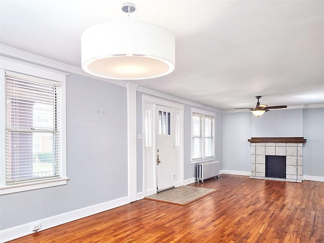 entrance foyer with hardwood / wood-style floors, a tile fireplace, radiator, ceiling fan, and ornamental molding