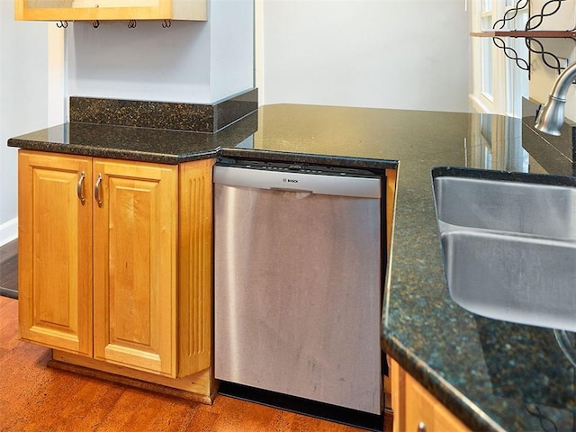 kitchen with dark stone countertops, hardwood / wood-style floors, stainless steel dishwasher, and sink