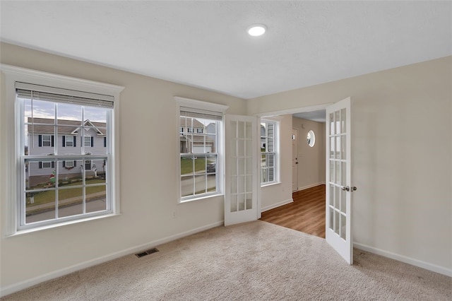 spare room with french doors, light colored carpet, and plenty of natural light