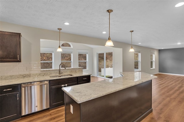 kitchen with light wood-type flooring, stainless steel dishwasher, sink, pendant lighting, and a center island