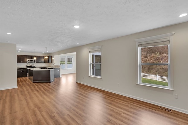 unfurnished living room featuring a healthy amount of sunlight, sink, a textured ceiling, and light hardwood / wood-style flooring