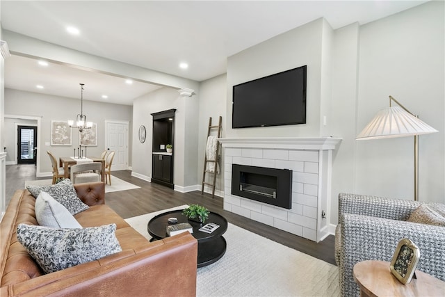 living room featuring a tiled fireplace, dark wood-type flooring, and an inviting chandelier