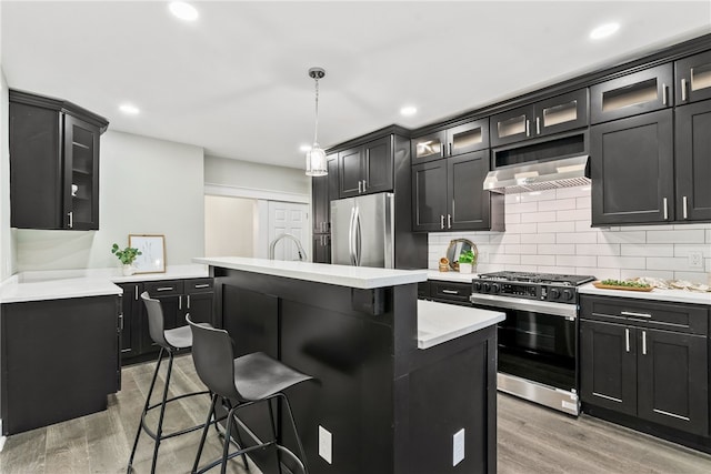 kitchen with light hardwood / wood-style floors, appliances with stainless steel finishes, decorative light fixtures, a kitchen island, and a kitchen bar