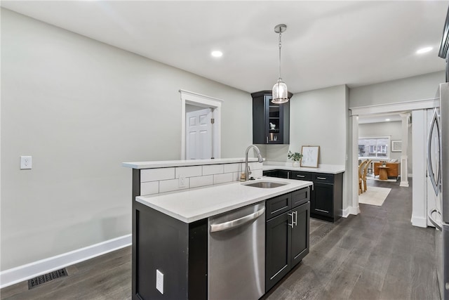 kitchen featuring dishwasher, sink, dark wood-type flooring, hanging light fixtures, and a kitchen island with sink