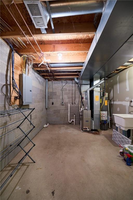 basement featuring gas water heater, sink, electric panel, and heating unit