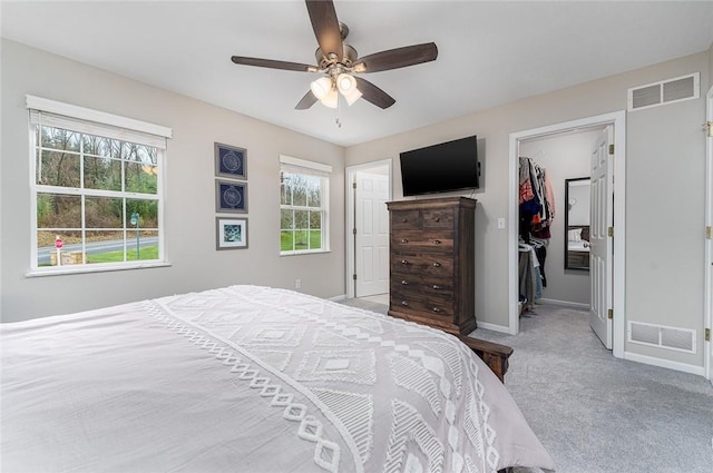 bedroom featuring light carpet, a walk in closet, a closet, and ceiling fan