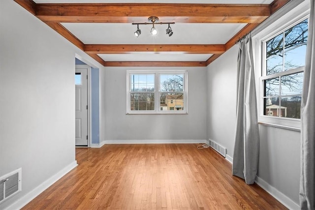 spare room featuring beamed ceiling, light hardwood / wood-style flooring, and a healthy amount of sunlight