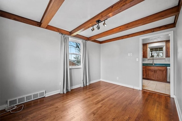 unfurnished room featuring sink, beamed ceiling, and light wood-type flooring