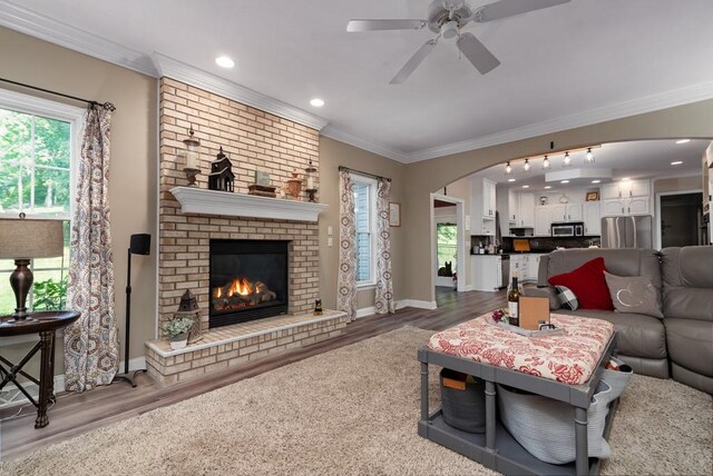 living room with a brick fireplace, crown molding, ceiling fan, and hardwood / wood-style flooring