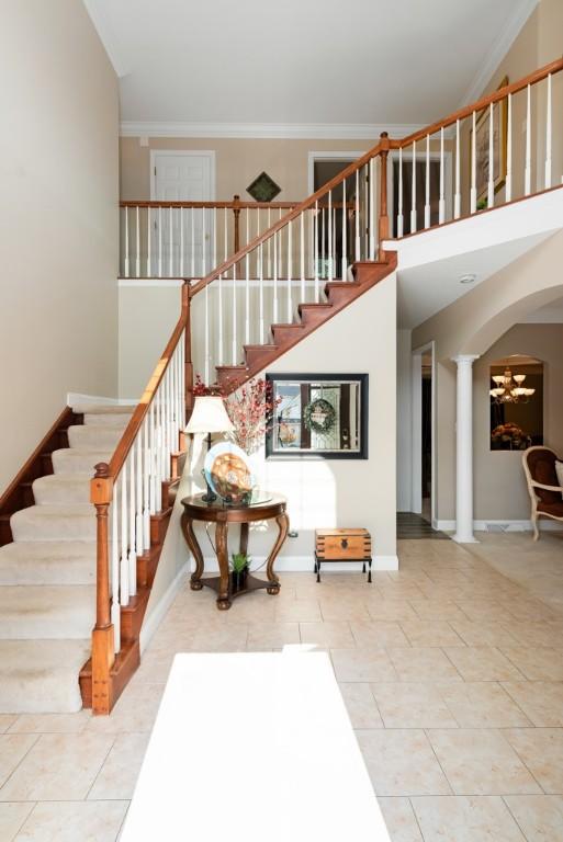 staircase featuring ornate columns, a notable chandelier, tile patterned floors, a towering ceiling, and ornamental molding