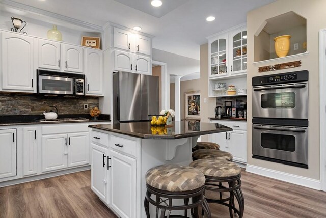 kitchen with a breakfast bar, white cabinets, wood-type flooring, and appliances with stainless steel finishes