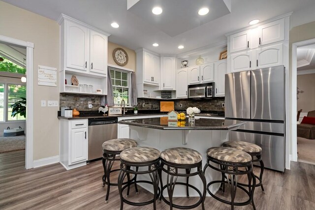 kitchen with appliances with stainless steel finishes, ornamental molding, white cabinets, a kitchen island, and a breakfast bar area